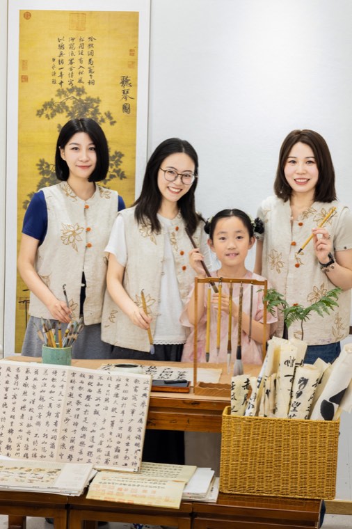 书院师生在木质书桌旁合影，墙面悬挂着书画，案头摆放笔架与纸张